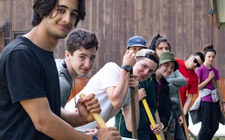 a group of students holding garden tools smile at the camera while doing a service project with outward bound